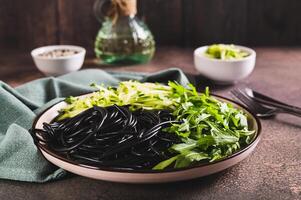 vegetarian maträtt svart spaghetti, gurka och arugula löv på en tallrik på de tabell foto