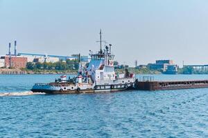 bogserbåt skjuter torr bulk frakt pråm på de flod i ett industriell landskap foto