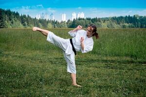 tonåring flicka Träning karate kata utomhus, utför de yoko geri sparka foto