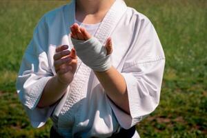 Tonårs flicka i en kimono omslag en handled slå in runt om henne hand innan tar karate utomhus foto