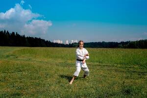 Tonårs flicka Träning karate kata utomhus, förbereder till prestera nedåt blockera gedan barai i zenkutsu dachi hållning foto