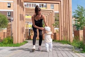 litet barn bebis flicka med mamma promenad i de stad gård, barn lär till promenad foto