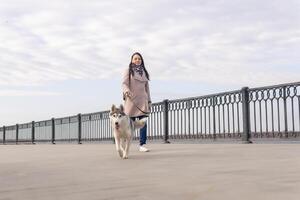 ung kvinna med en hes hund promenader längs de vägbank i ett höst dag foto