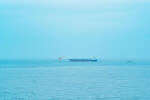 dimmig marinmålning med en tankfartyg nära ett olja terminal belägen långt ut till hav foto