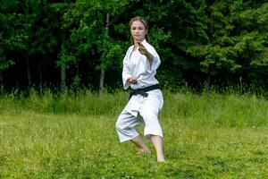 Tonårs flicka Träning karate kata utomhus, utför soto uke eller utanför blockera i kakutsu dachi stå foto