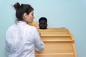 ung svart man tar en terapi session i en fyto tunna under de övervakning av läkare foto