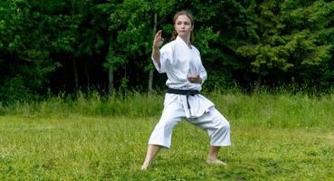 Tonårs flicka Träning karate kata utomhus, utför soto uke eller utanför blockera i kakutsu dachi stå foto