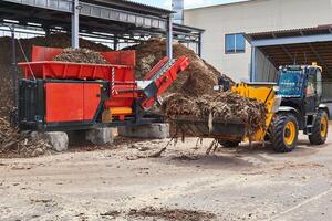 hink lastare massor träd bark in i ett industriell flishugg foto