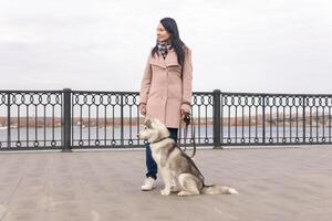 ung kvinna med en hes hund gående på de stad vägbank i ett höst dag foto