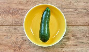 grön zucchini squash med mönstrad hud på en gul tallrik på en trä- bordsskiva foto