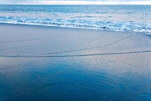 hav strand med en Vinka kommande tillbaka, i som de himmel är reflekterad foto