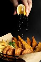 fisk och pommes frites på svart bakgrund med stänk citron- på hand foto