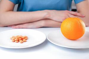 där är en mogen orange på de ett tallrik och vitamin c tabletter på annan ett. val mellan naturlig och syntetisk sätt av hälsa vård. friska livsstil begrepp. närbild. foto