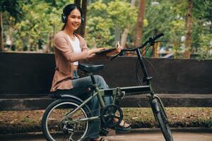 Lycklig ung asiatisk kvinna medan ridning en cykel i en stad parkera. hon log använder sig av de cykel av transport. miljömässigt vänlig begrepp. foto