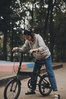 Lycklig asiatisk ung kvinna promenad och rida cykel i parkera, gata stad henne leende använder sig av cykel av transport, eco vänlig, människor livsstil begrepp. foto