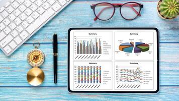 företag analys begrepp, en läsplatta med data diagram vilar på en blå trä- skrivbord, kompletteras förbi en årgång kompass, glasögon, och tangentbord, illustrerar de navigering av företag trender. foto
