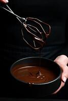 svart skål med mörk varm choklad i händer. kök redskap. på en svart bakgrund. foto