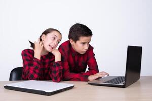 liten flicka rörande henne hår och pojke använder sig av en dator på skola foto