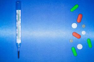 medicinsk termometer och Färg piller på en blå bakgrund. sjukvård och först hjälpa begrepp. foto