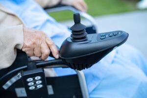 asiatisk senior kvinna patient på elektrisk rullstol med joystick och avlägsen kontrollera på sjukhus. foto