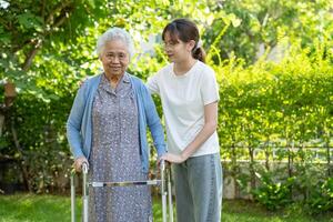 vårdgivare hjälp asiatisk äldre kvinna patient promenad med rollator i parkera, friska stark medicinsk begrepp. foto