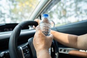 asiatisk kvinna förare håller flaska för att dricka vatten medan du kör bil. varmvattenflaska i plast orsakar brand. foto