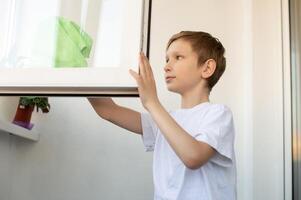 en söt pojke är rengöring, tvättning ett öppen fönster på de balkong. foto