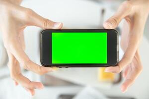 närbild hand innehav smartphone topp se i restaurang med tom Plats grön skärm färgad foto