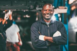 porträtt garage mekaniker professionell arbetstagare bil motor service ser kamera leende ärm korsade foto