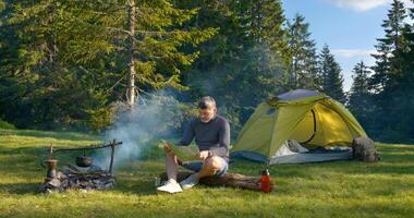 skäggig man nära lägereld i de skog. de camping är belägen i en skön skog gräsmatta i de berg. resa begrepp foto