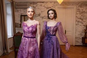 två kvinnor i lila klänningar stå i en rum foto