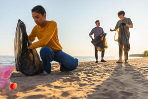 jord dag. volontärer aktivister samlar sopor rengöring av strand kust zon. kvinna och mannens sätter plast skräp i sopor väska på hav Strand. miljö- bevarande kust zon rengöring foto