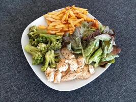 hemlagad grillad kyckling med franska pommes frites, broccoli och grön sallad, eras på en vit tallrik foto