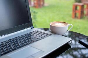 bärbar dator med latte varm kaffe i vit kopp på glas tabell foto
