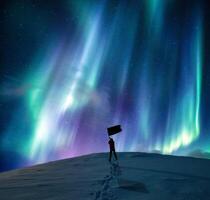 aurora borealis över silhuett Lycklig man stående vinka flagga på snöig berg i arktisk cirkel på vinter- foto