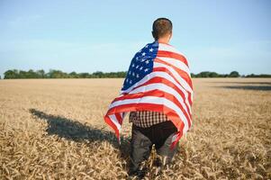 ung man innehav amerikan flagga, stående i vete fält foto