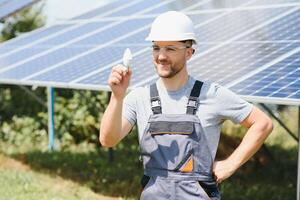 teknisk expert- i sol- solceller paneler, avlägsen kontrollera utför rutin- insatser till övervaka de systemet använder sig av rena förnybar energi i de hand en ljus Glödlampa. foto