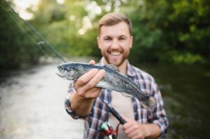 Lycklig fiskare innehav en fisk fångad. fiske på de skön flod. foto