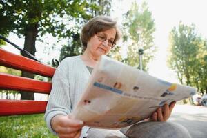 vuxen kvinna Sammanträde i parkera och läsning tidningar. foto