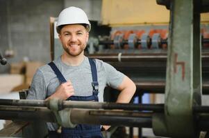 leende och Lycklig anställd. industriell arbetstagare inomhus i fabrik. ung tekniker med vit hård hatt. foto