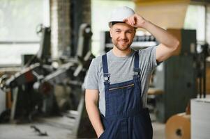 leende och Lycklig anställd. industriell arbetstagare inomhus i fabrik. ung tekniker med vit hård hatt. foto