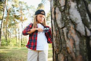 bak- se bild av söt liten flicka utforska de natur med förstorande glas utomhus. barn spelar i de skog med förstorande glas. foto