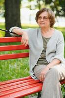äldre kvinna Sammanträde och avkopplande på en bänk utomhus i parkera foto