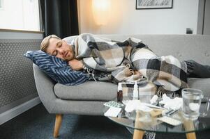 sjuk skäggig man vem har dålig kall eller säsong- influensa Sammanträde på soffa på Hem. kille med feber bär värma pläd skakningar med orolig ansikte uttryck. foto