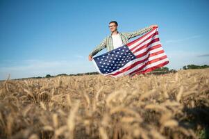 ung patriotisk jordbrukare står bland ny skörda. pojke gående med de amerikan flagga på de vete fält fira nationell oberoende dag. 4:e av juli begrepp. foto