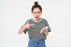 arg kvinna klagar, pekande på smartphone och skrikande med frustrerad ansikte uttryck, isolerat över vit bakgrund foto