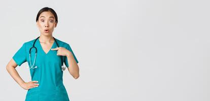 covid19, sjukvård arbetare, pandemi begrepp. överraskad och bakhåll asiatisk kvinna läkare, sjuksköterska i scrubs pekande på själv, beaing som heter eller utvalda, stående vit bakgrund foto