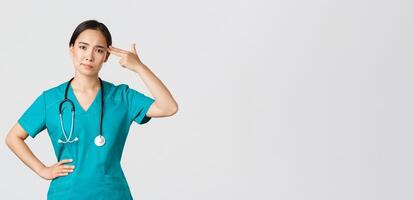 covid19, sjukvård arbetare, pandemi begrepp. utmattad och besvärad, irriterad asiatisk kvinna läkare, sjuksköterska framställning skott pistol gest över huvud från leda, vit bakgrund foto