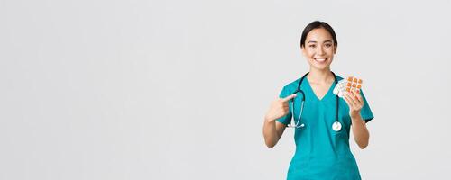 sjukvård arbetare, förebyggande virus, karantän kampanj begrepp. leende vänlig kvinna läkare, sjuksköterska i scrubs pekande finger på vitaminer eller biljard, som visar medicin, vit bakgrund foto