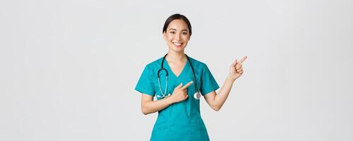 covid19, sjukvård arbetare, pandemi begrepp. leende skön asiatisk kvinna sjuksköterska, internera pekande fingrar övre rätt hörn, inbjudande för kolla upp, uppkopplad klinik utnämning, vit bakgrund foto